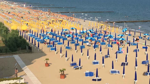 A beach with rows of blue and orange umbrellas, a sandy walkway, and a clear view of the sea.