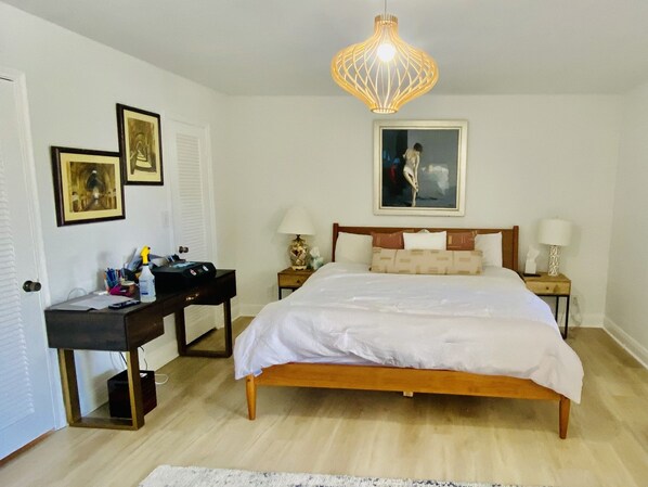 A bedroom with a wooden bed, white bedding, a desk with a lamp, and a painting on the wall.