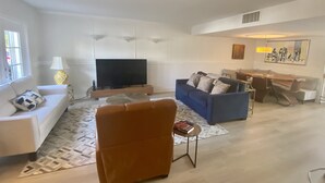 A modern living room with a sofa, a coffee table, a TV, and a dining area with chairs and a table. - Lovely two story home on the water (Hallandale Beach)