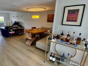Un salon moderne avec une table à manger en bois, des sièges confortables, une table basse en verre et un téléviseur fixé au mur.