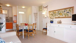A dining area with a table set for four, surrounded by wooden chairs with blue cushions. There is a white cabinet with a television on top.