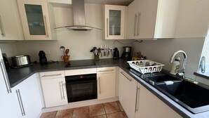 A compact kitchen with white cabinets, a stainless steel range hood, a dishwasher, and a sink with a faucet. - Charming Penty Breton, close to the beaches and town of Tregunc - 6 people max. (Trégunc)