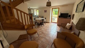 A dining area with a table and chairs, a kitchen in the background, a staircase, and a television on a cabinet. - Charming Penty Breton, close to the beaches and town of Tregunc - 6 people max. (Trégunc)