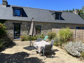 Una casa de piedra con techo de tejas, un patio con mesa y sillas, y un pequeño jardín.