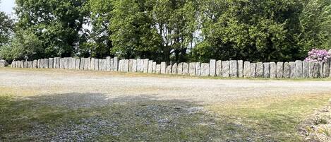 A gravel path leading to a stone wall with trees in the background.