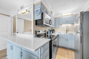 A modern kitchen with a central island, stainless steel appliances, and light blue cabinetry.