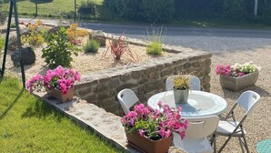 Eine Gartenpatio mit Steinmauer, Pflanzgefäßen und weißen Stühlen.
