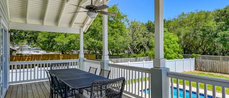 A covered outdoor patio with a pool, wooden deck, and white railings.