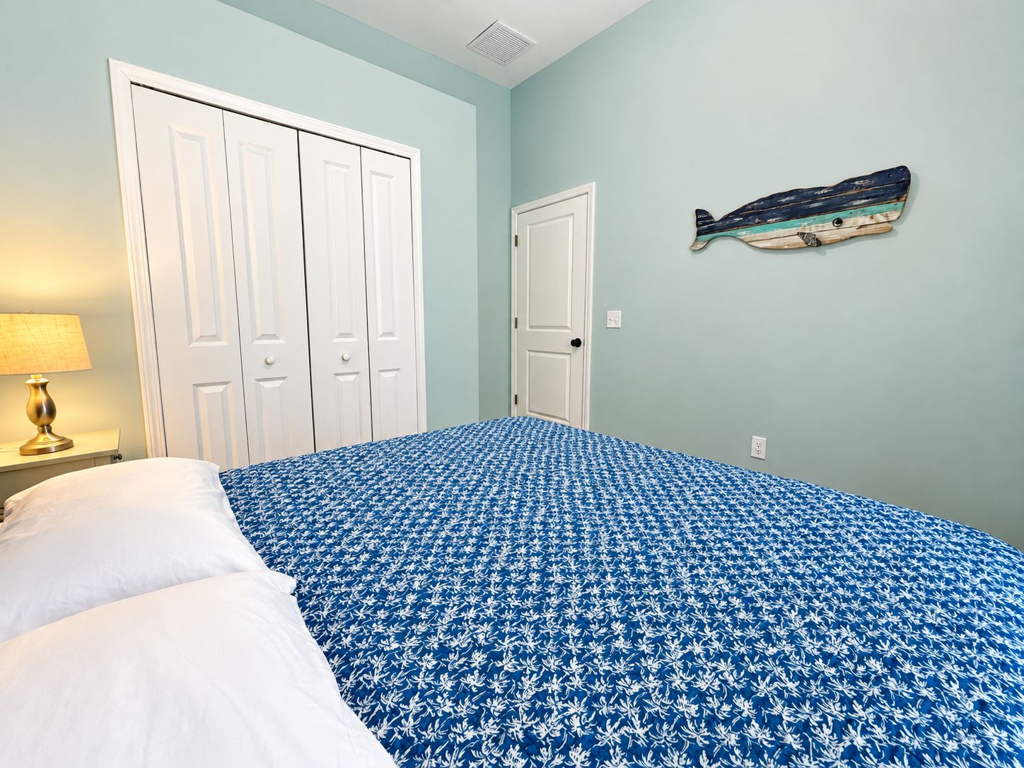 Une chambre à coucher avec un lit, deux portes blanches, une œuvre d’art accrochée au mur et une lampe.
