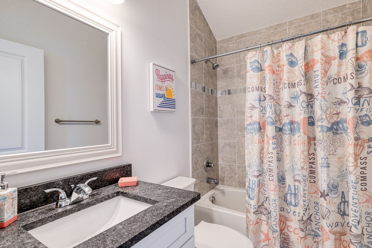 Une salle de bain avec un grand miroir, un lavabo et un rideau de douche orné de motifs marins.