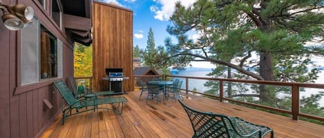 A wooden deck with outdoor furniture, a grill, and a view of the lake.
