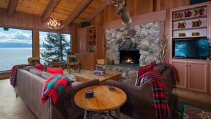 A cozy living room with a stone fireplace, wooden beams, a mounted deer head, and a view of the lake. - Lakefront Retreat in Tahoe City- large home in Dollar Point (Tahoe City)