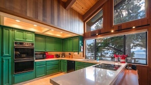 A modern kitchen with green cabinets, a large island, and a view of the outdoors. - Lakefront Retreat in Tahoe City- large home in Dollar Point (Tahoe City)