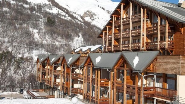 Un chalet en bois doté de plusieurs balcons et offrant une vue sur des montagnes enneigées.
