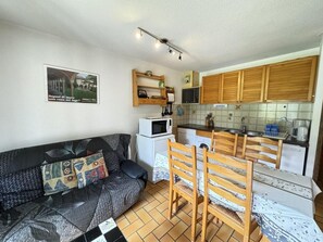 A compact living space with a sofa, dining table, chairs, a microwave, a small refrigerator, and wooden cabinets. - 300m from resort center, 1st floor, balcony, tv, 32m², Serre Chevalier (Le Monêtier-les-Bains)
