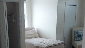 Un dormitorio con una cama, una silla, una mesita y una puerta.