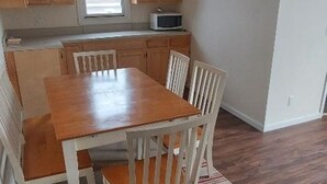 Una cocina con armarios de madera, una mesa de comedor con sillas, un microondas y un ventanal.