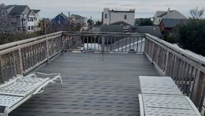 Una terraza de madera con dos sillones blancos de metal y un objeto pequeño negro en el centro.