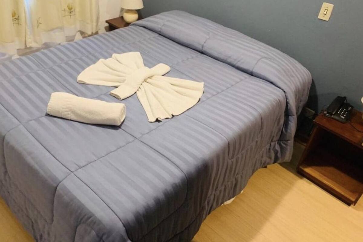 Ein ordentlich bezogenes Bett mit einer blau gestreiften Tagesdecke und einem in Fächerform drapierten Handtuch.