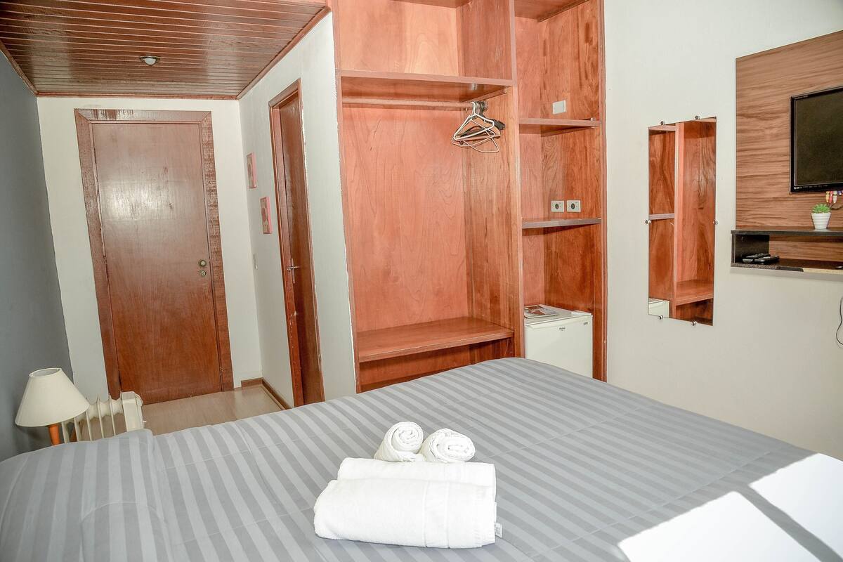 Ein Hotelzimmer mit einem Bett, einem Holzschrank, einem Fernseher und einer kleinen Topfpflanze.