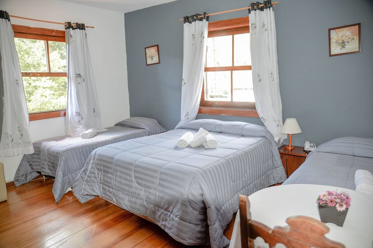 Ein Zimmer mit zwei Betten, Holzboden und einem kleinen Tisch mit Blumen in einer Vase.