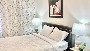 Un dormitorio ordenado con cama, ventilador de techo, una obra de arte enmarcada y lámparas de noche.