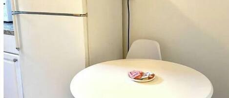 Una cocina pequeña con un refrigerador blanco, una mesa blanca con un plato de comida y un cuadro colgado en la pared.