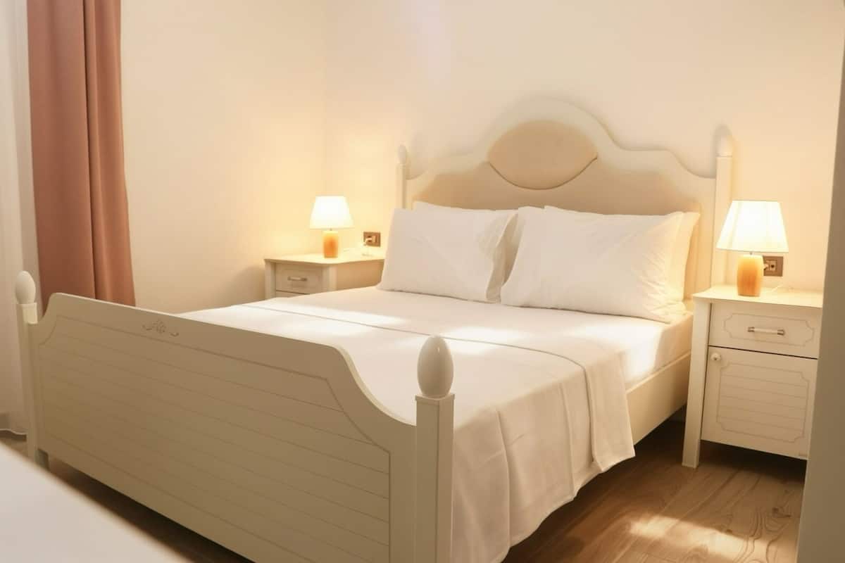A neatly made bed with white linens, two bedside tables with lamps, and a wooden floor.