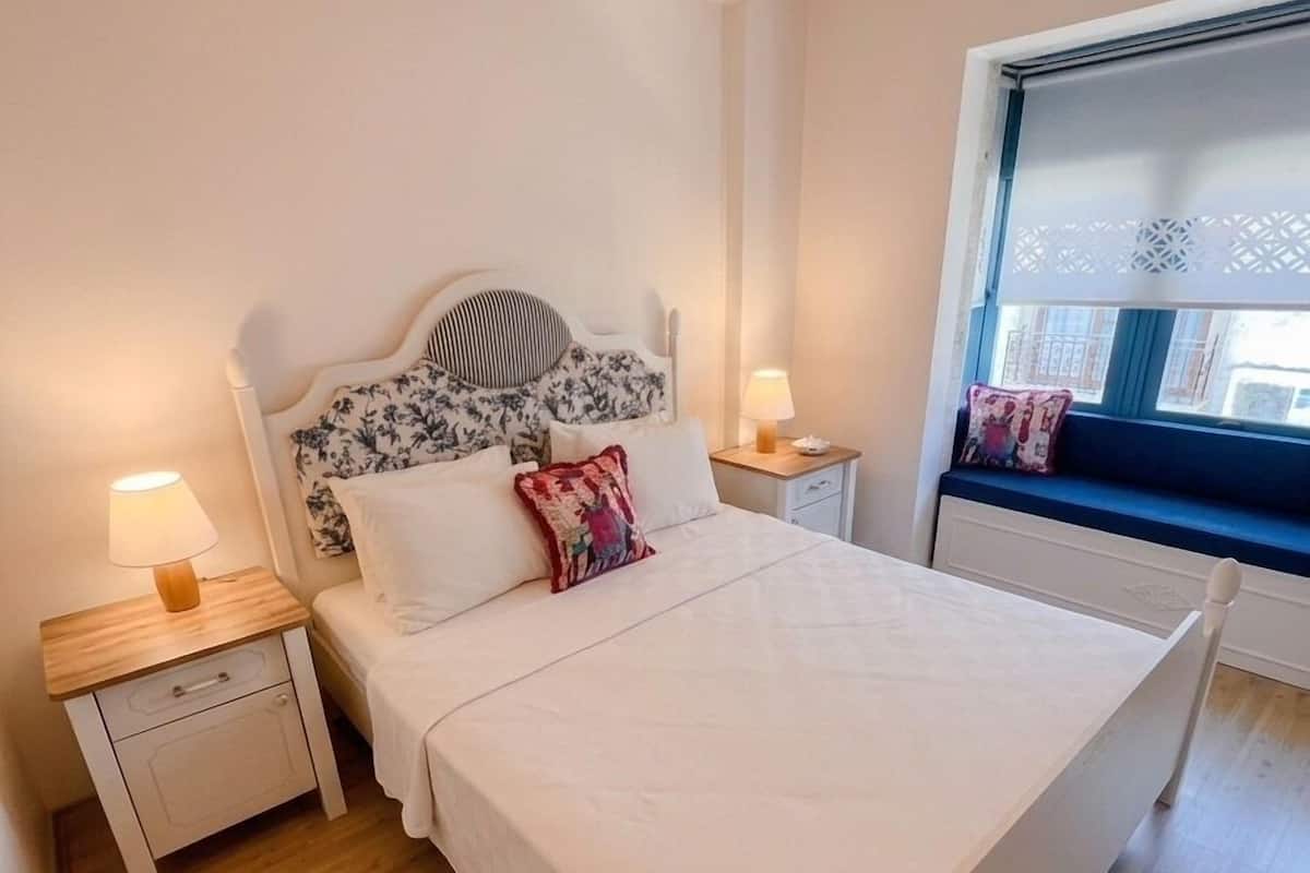 A bedroom with a bed, two bedside tables, a window with a view, and a wooden floor.