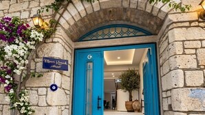 A stone building with a blue door, a sign reading 'Mari Konole Apartments,' and a potted plant inside. - Mavi Konak Alacati (Cesme)
