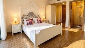 A bedroom with a bed, bedside tables, a nightstand, a wardrobe, and a shower area. - Mavi Konak Alacati (Cesme)