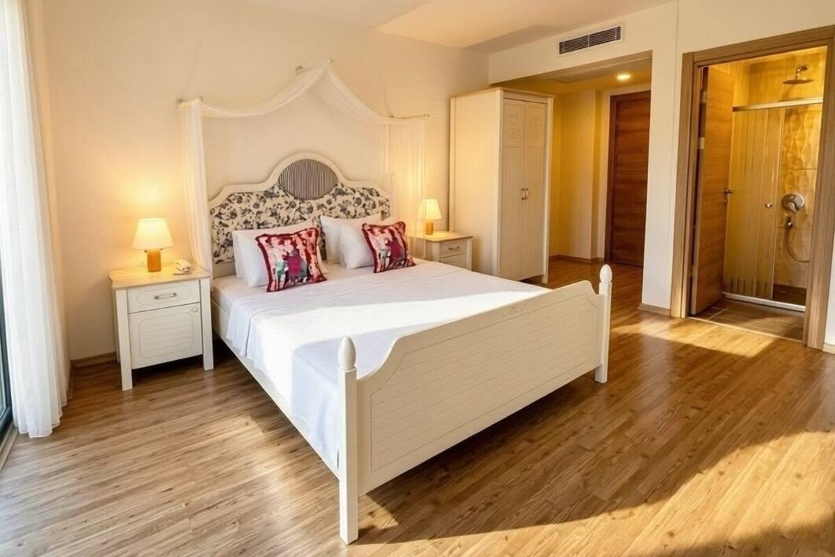 A bedroom with a bed, bedside tables, a nightstand, a wardrobe, and a shower area.