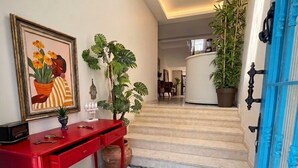 A hallway with a geometric patterned floor, a red console table with decorative items, a framed artwork, and a staircase leading to another room. - Mavi Konak Alacati (Cesme)