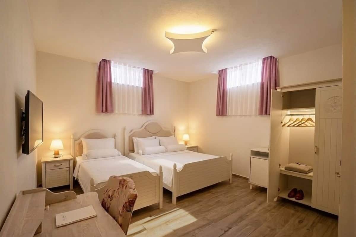 A hotel room with two beds, a desk, a wardrobe, and a mirror.