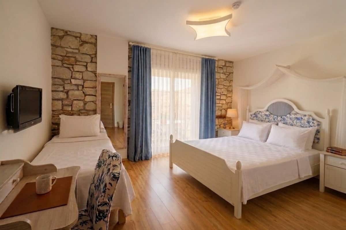 A hotel room with two beds, a television, a stone wall, and a wooden floor.