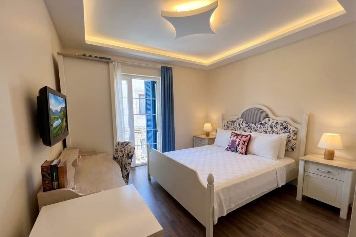 A bedroom with a bed, bedside tables, a desk, a chair, and a TV mounted on the wall.