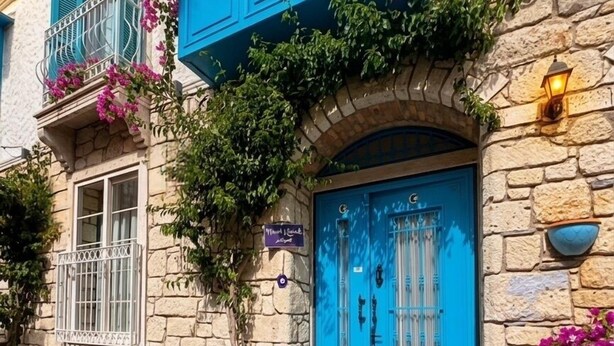 A stone building with a blue door and shutters, a small table with chairs, and potted plants. - Mavi Konak Alacati (Cesme)
