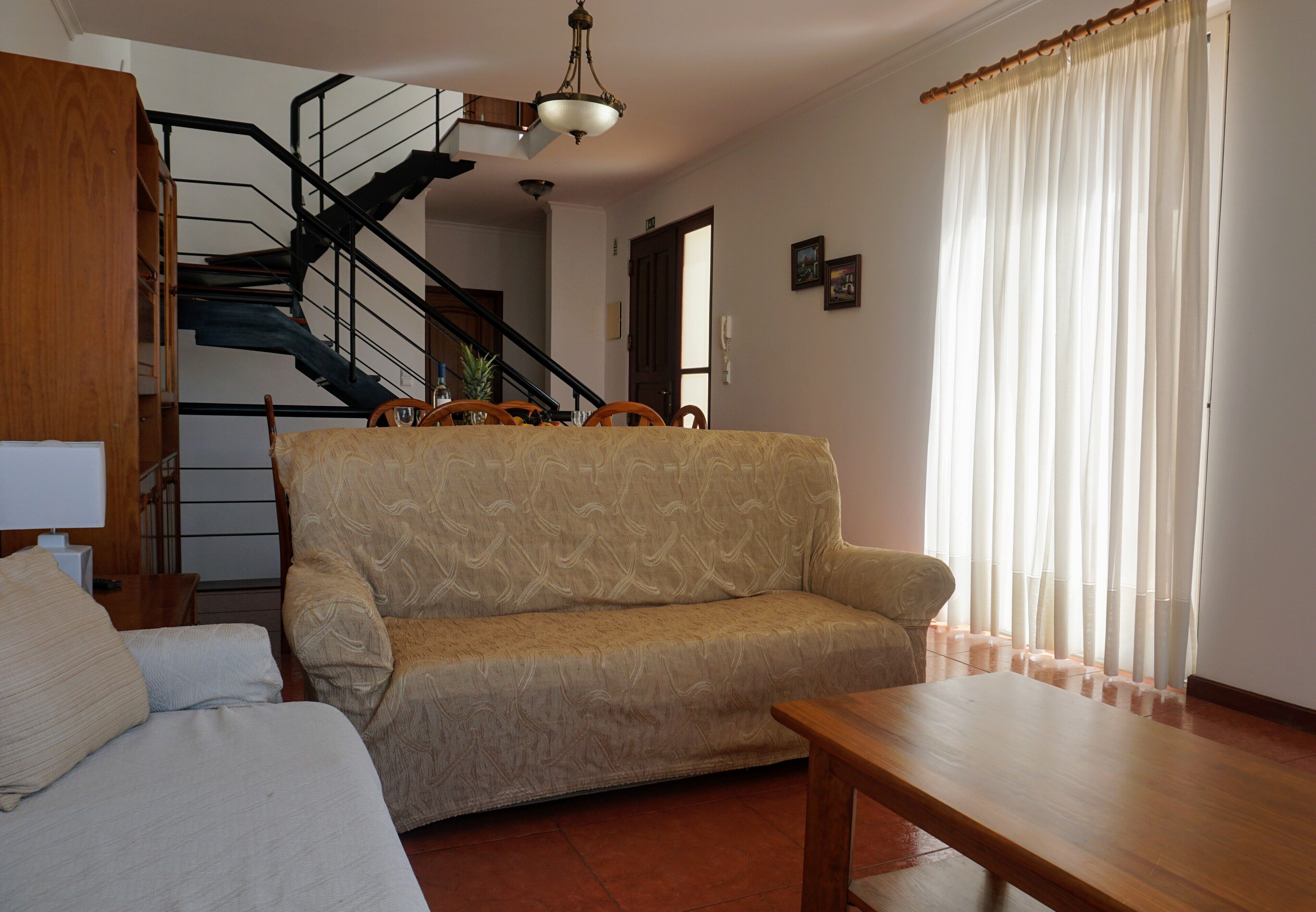 Un saló amb un sofà, una taula de centre de fusta, una escala i una porta que dona a una altra habitació.