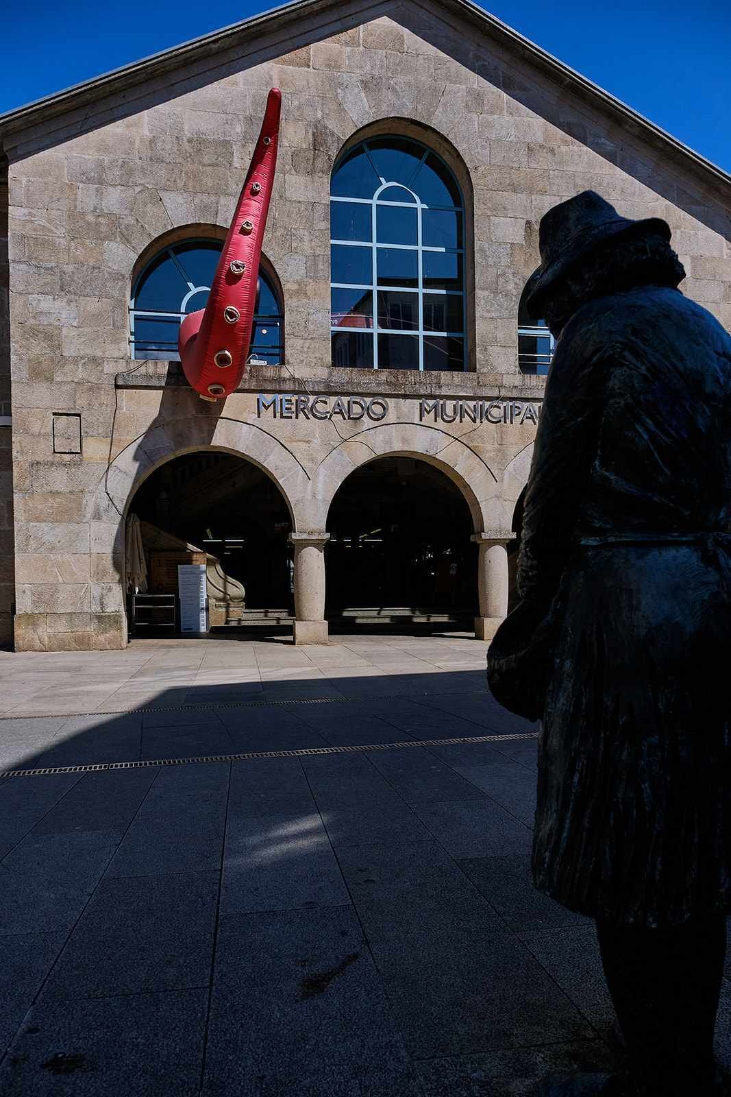 Um edifício com a inscrição 'MERCADO MUNICIPAL' e uma estátua de uma pessoa em frente.
