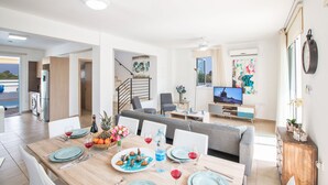A modern living room with a dining area, a sofa, and a television. - Protaras Holiday Villa Kv60 (Pernera)