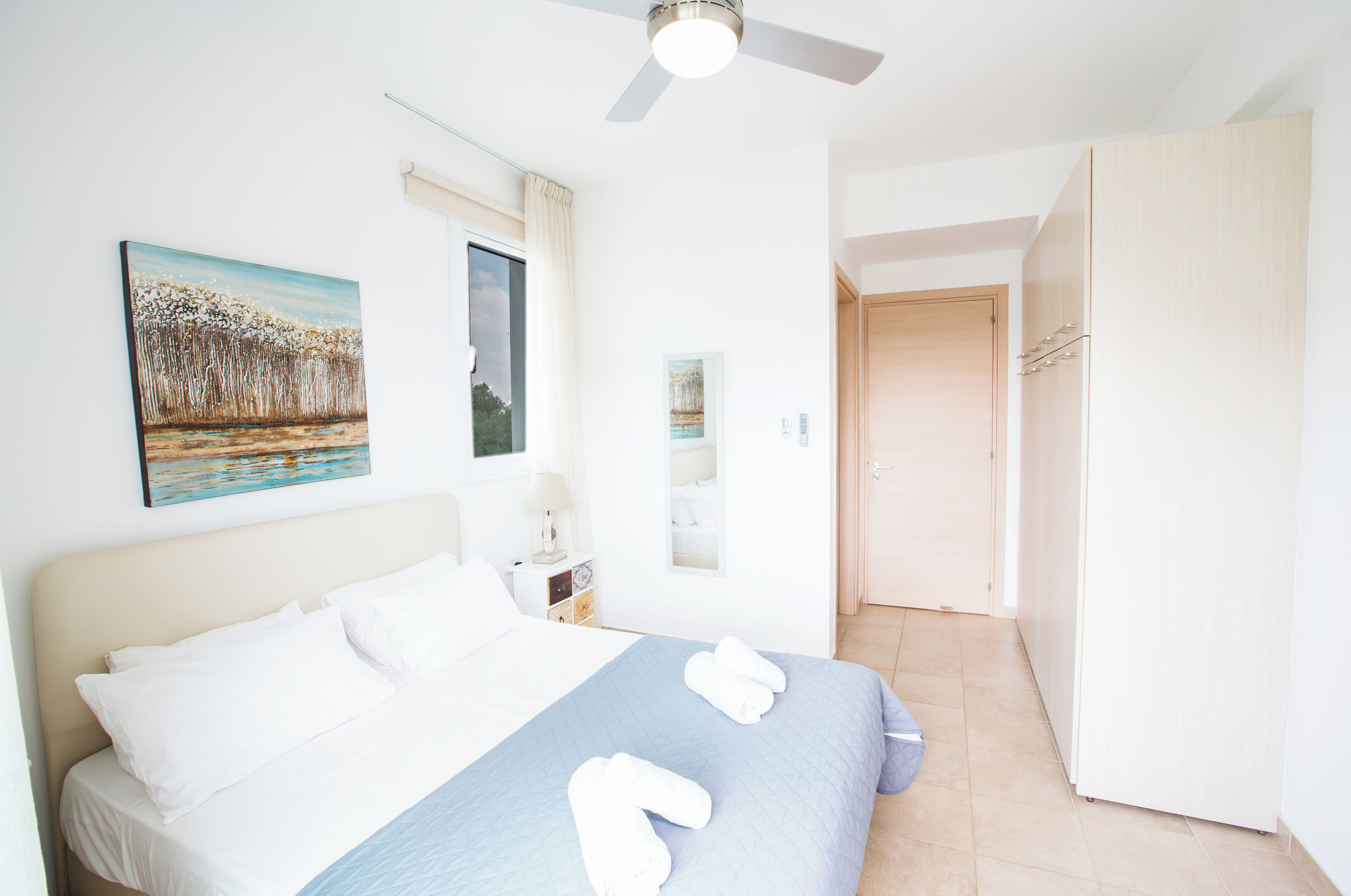 Une chambre à coucher avec un lit, un ventilateur de plafond, une table de chevet et un tableau accroché au mur.