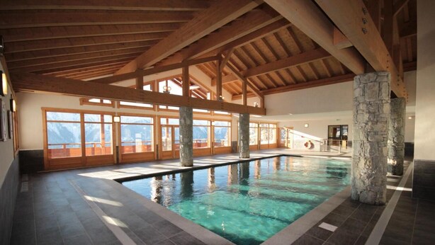 Indendørs swimmingpool med stensøjler, træbjælker og store vinduer med udsigt til bjerge.