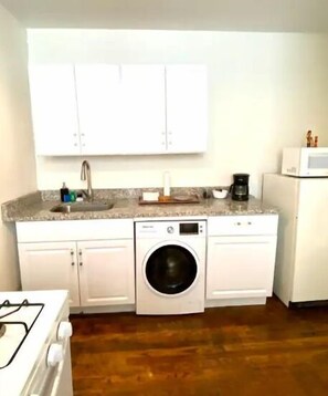 A compact kitchen with white cabinets, a built-in washing machine, a microwave, and a coffee maker.