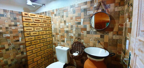 Un baño con pared de azulejos estampados, inodoro, lavamanos con recipiente grande y espejo colgante.