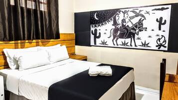 Une chambre à coucher comprenant un lit, une table de chevet, une œuvre d’art accrochée au mur représentant un paysage désertique, et une fenêtre avec des rideaux.
