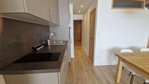 Et køkken med moderne design, mørk bordplade, stålvask og et træspisebord.