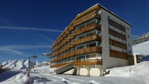 Et hotel med flere etager og træbalkoner, foran et sneklædt bjerg.