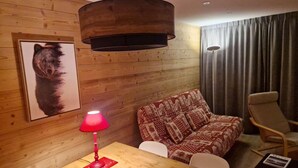 Et værelse med træpaneler, en sofa med et mønster, et bord med en rød lampe og en stol.