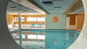 En indendørs swimmingpool med flisegulv, trævægge og to blå liggestole.
