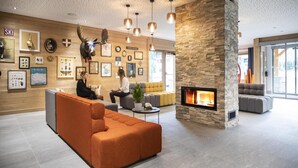 A modern lobby with a stone fireplace, wooden walls, and a seating area with orange sofas. - Wifi, swimming pool, terrace, balcony, tv, ski locker, 43-61m², Samoëns (Samoëns)